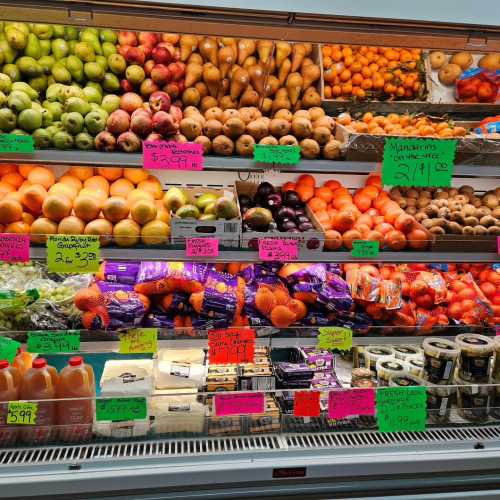 A colorful display of various fruits and vegetables with price tags, including apples, oranges, and potatoes.