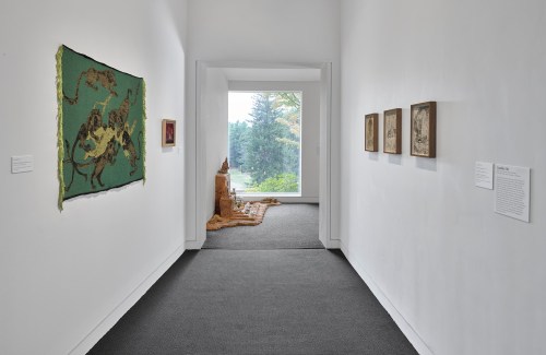 A gallery hallway featuring artwork on the walls and a view of nature through a large window at the end.