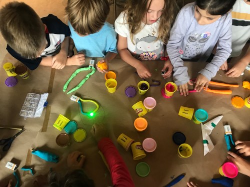 Children engaged in a creative activity with colorful playdough and various tools on a table.