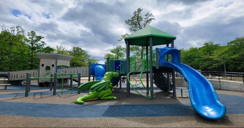 A colorful playground featuring a green dragon sculpture, slides, and climbing structures under a cloudy sky.