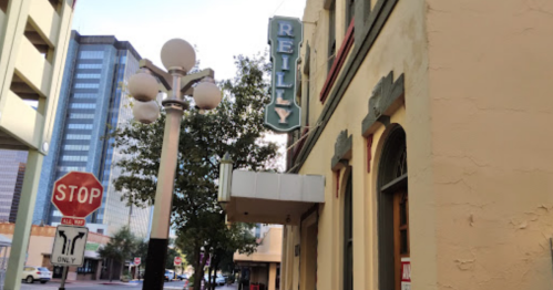 A street view of a building with a "Reilly" sign and a stop sign nearby, surrounded by urban architecture.
