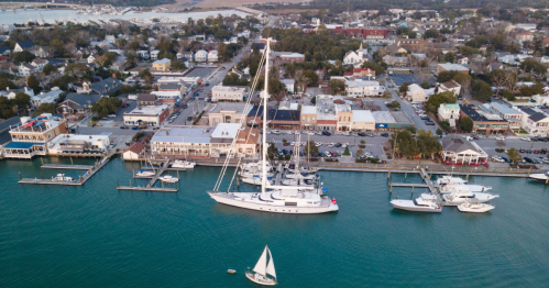 Aerial view of a coastal town with boats in the harbor, shops lining the waterfront, and a marina in the background.