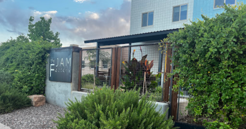 Sign for "The Jam Factory" surrounded by greenery and a modern building in the background.