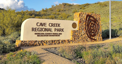 Sign for Cave Creek Regional Park, featuring stone design and surrounded by desert vegetation under a blue sky.