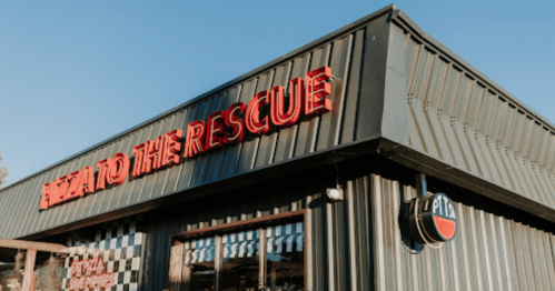 Sign on a building reads "Pizza to the Rescue," with a checkered pattern and a round logo on the side.