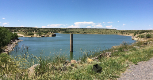 A serene lake surrounded by greenery and rocky shores under a clear blue sky.