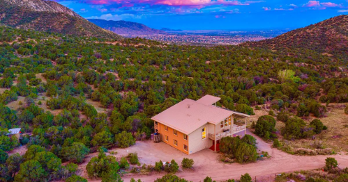 Aerial view of a house surrounded by lush greenery and mountains under a colorful sunset sky.