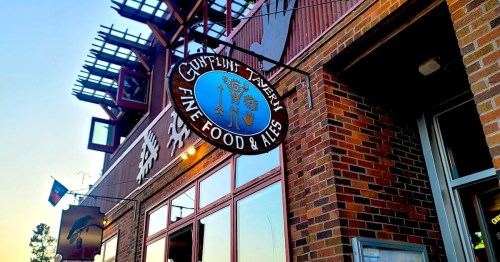Sign for "Coyote Tavern" featuring "Fine Food & Ales" against a brick building at sunset.