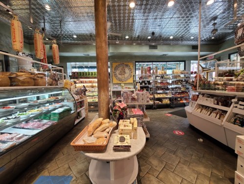 A vibrant grocery store interior featuring displays of meats, cheeses, and various packaged goods.