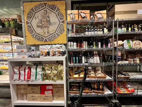 A grocery store display featuring shelves of oils, snacks, and a mosaic art piece on the wall. A scooter is nearby.