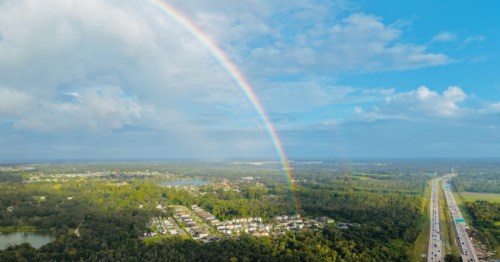 An aerial view of a bright rainbow over a Florida highway and lush green landscape.
