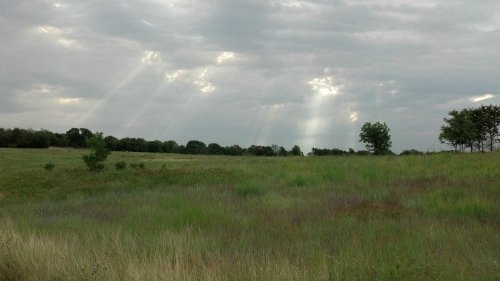 A grassy field under a cloudy sky, with rays of sunlight breaking through the clouds.