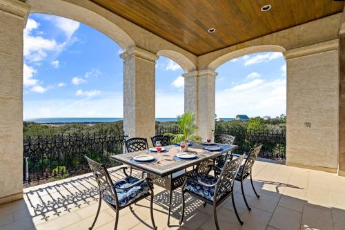 A spacious outdoor dining area with a table set for six, overlooking a scenic view of trees and the ocean.