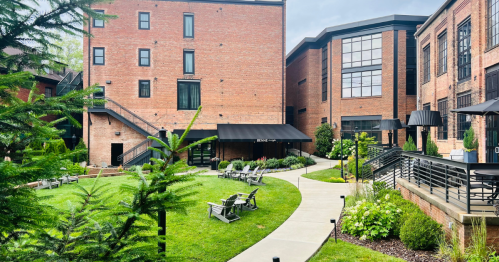 A landscaped courtyard with a pathway, lounge chairs, and brick buildings in the background. Greenery surrounds the area.