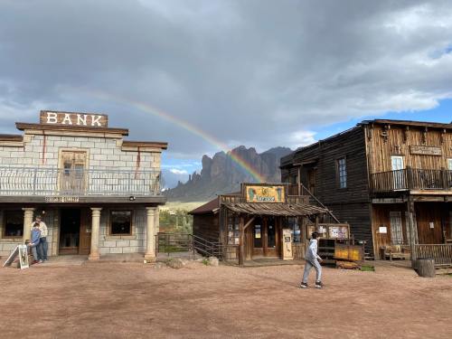 A western-style town with a bank, shops, and a rainbow in the sky, set against rocky mountains.