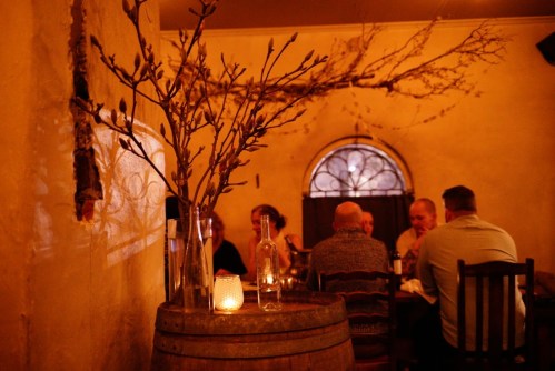 A cozy restaurant scene with a candlelit table, a decorative branch, and diners enjoying their meal in warm lighting.