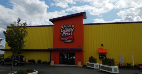 Exterior of Grand Prix Family Fun Center, featuring bright orange and yellow walls, with a logo and cloudy sky above.