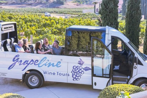 A group of people enjoying a wine tour in a Grapeline shuttle bus amidst a vineyard.