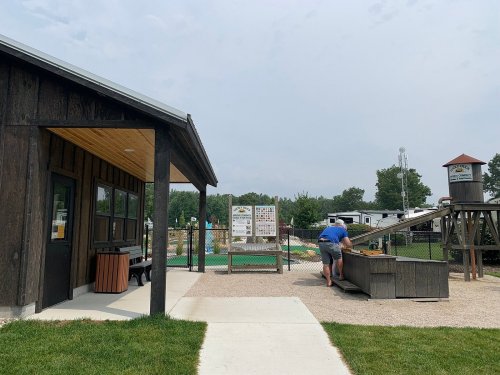 A man interacts with a wooden structure near a recreational area with a water slide and grassy surroundings.