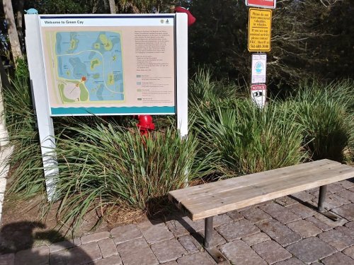 A park map sign at a nature area with a wooden bench and lush greenery surrounding it.