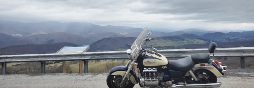 A motorcycle parked on a scenic overlook with mountains and cloudy skies in the background.
