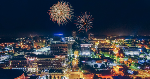 A vibrant city skyline at night with colorful fireworks lighting up the sky above.