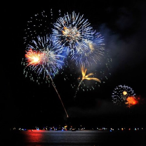 Colorful fireworks burst in the night sky over a calm body of water, reflecting vibrant lights below.
