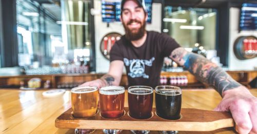 A smiling bartender presenting a tray of four different craft beer samples inside Straight to Ale speakeasy in Huntsville, Alabama.