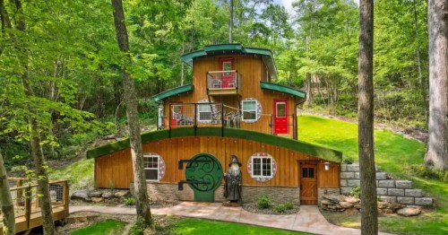 Multi-story wooden "hobbit" house in the woods featuring a Gandalf statue and a round green door.