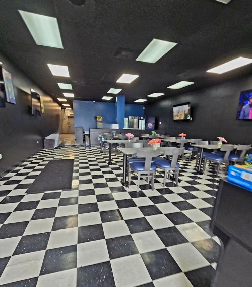 Interior of a restaurant featuring black and white checkered flooring, tables with blue chairs, and wall-mounted TVs.