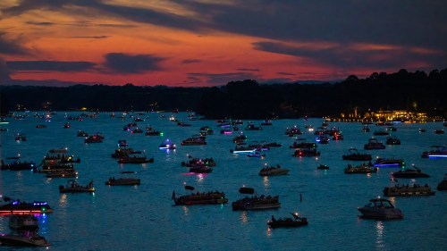 A vibrant sunset over a lake filled with boats, illuminated by colorful lights, creating a festive evening atmosphere.