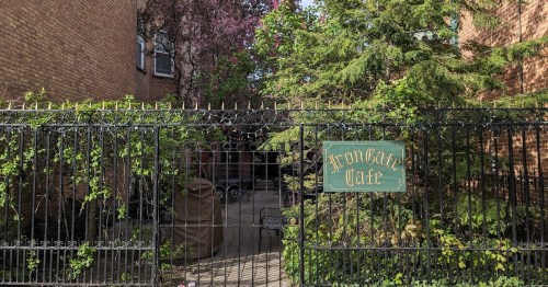 A wrought iron gate with "Iron Gate" sign, surrounded by greenery and brick buildings in a quiet setting.