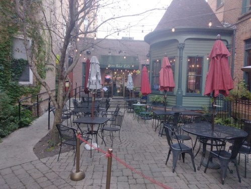 Outdoor seating area of a café with red umbrellas, surrounded by greenery and a charming building in the background.