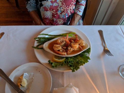 A plate of shrimp with asparagus and lettuce, served on a white tablecloth with utensils nearby.