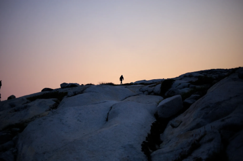 Silhouette of a person walking on rocky terrain against a colorful sunset sky.