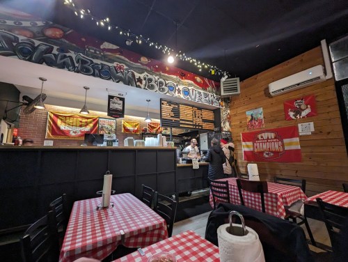 Interior of a casual restaurant with checkered tables, a counter, and graffiti art on the walls. Staff are serving customers.