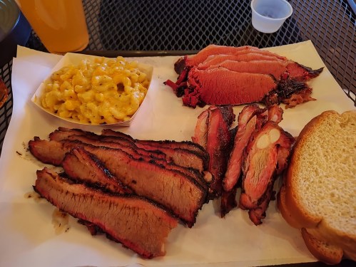 A plate of smoked brisket, sliced turkey, macaroni and cheese, and bread on a tray.