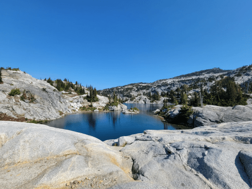 A serene lake surrounded by rocky terrain and pine trees under a clear blue sky.