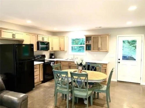Modern kitchen with wooden cabinets, black appliances, a round dining table, and a door leading outside.