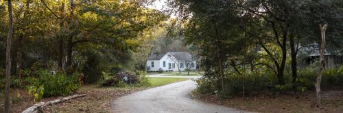 A winding path leads to a white house surrounded by trees and greenery in a serene, rural setting.
