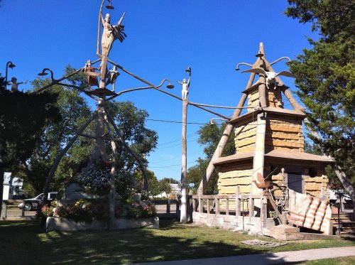 A unique outdoor sculpture featuring figures and structures, surrounded by greenery and a clear blue sky.