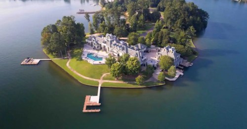 Aerial view of a large mansion on a private island surrounded by water and lush greenery.