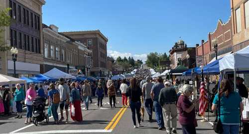 A bustling street market with tents and crowds, set against a backdrop of historic buildings and a clear blue sky.