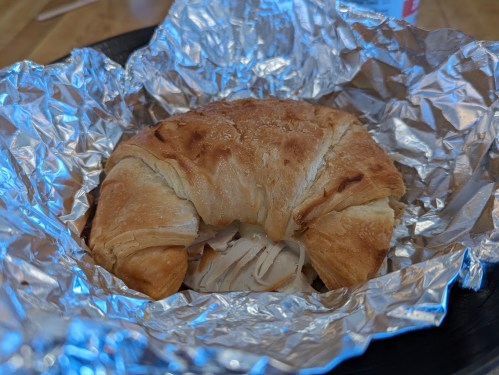 A golden-brown croissant wrapped in foil, filled with sliced turkey.