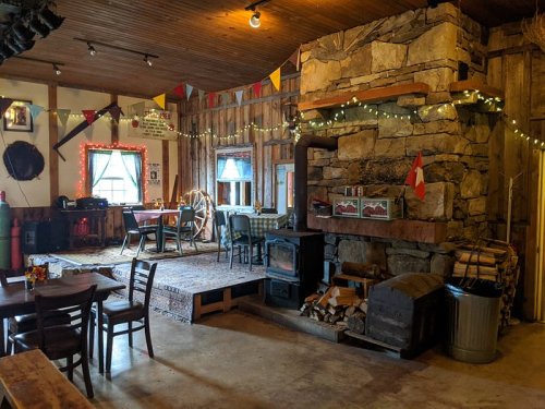 Cozy interior of a rustic cabin with a stone fireplace, wooden tables, and festive decorations.