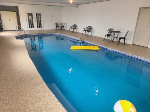 Indoor swimming pool with a yellow float, beach ball, and chairs around the edge. Bright and inviting atmosphere.