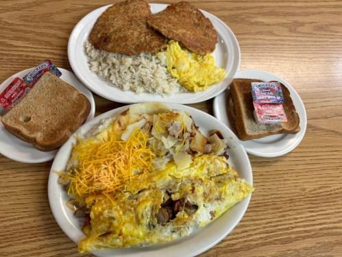 A plate of omelette with cheese and potatoes, served with toast and a side of rice and two breaded patties.