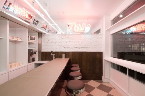 A modern diner interior with a long counter, stools, and neon signs, featuring a minimalist design and warm lighting.