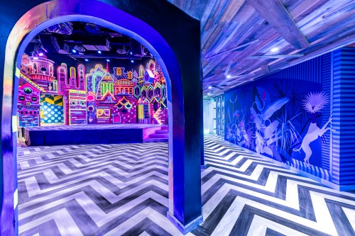 Vibrant interior of a venue featuring colorful murals, a stage, and a striking chevron-patterned floor.