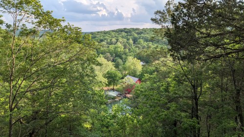 A scenic view of lush green trees and a red barn nestled in a valley, under a partly cloudy sky.